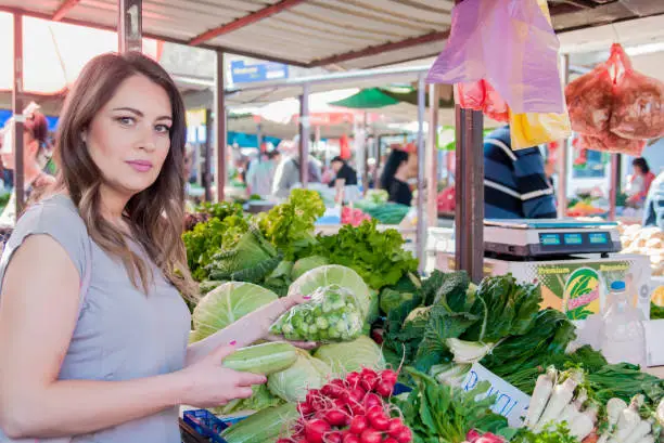 Glad female customer holding fresh cabbage-head on market. Pretty young woman buying vegetables on the market