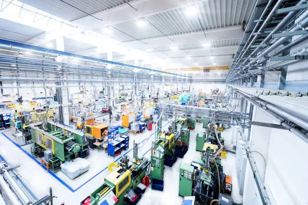 Horizontal high angle view color image of futuristic factory. Industrial aisle surrounded by modern machines which having busy robotic arms with molding shapes and producing plastic pieces for variety of industry. Labor intensive production line with manufacturing equipment - boxes, crates, crane, packages, pallets, space for copy
