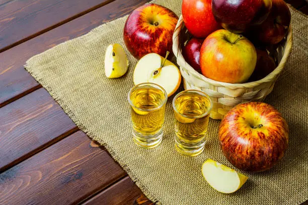 Apple brandy shots and red apples in the rustic wicker basket on wooden background