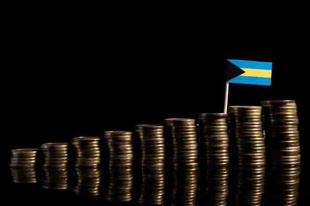 Photo of Bahamas flag with lot of coins isolated on black background