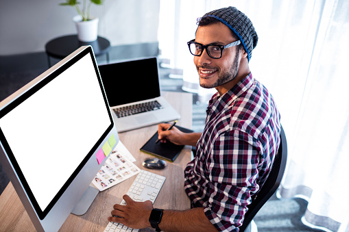 Smiling hipster man posing for camera while sitting at computer desk in office
