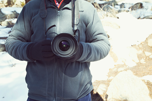 Midsection of photographer in warm clothing holding SLR camera