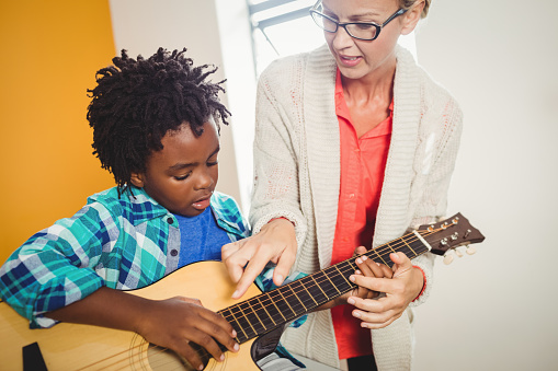 Boy learning how to play the guitar with the help of a teacher
