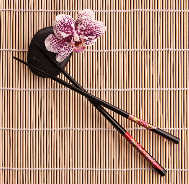 Chopsticks with black stone and orchid flower on a bamboo table mat