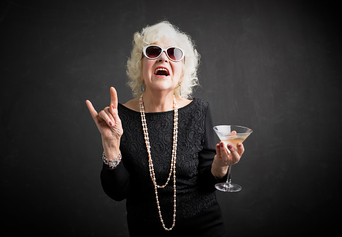 Cool grandmother with sunglasses and drink in hand showing rock sign