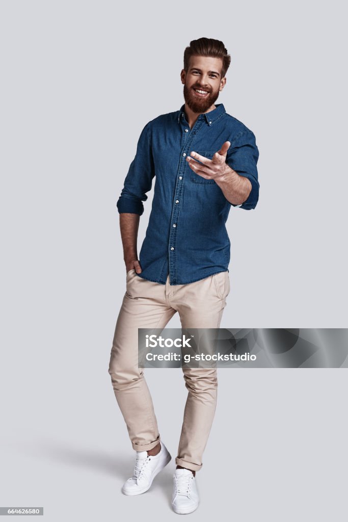 You are the one I need! Full length of handsome young man pointing you and keeping hand in pocket while standing against grey background Men Stock Photo