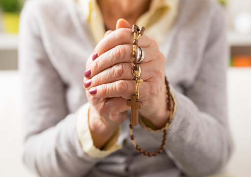 Grandma holding wooden rosary in hands  and praying