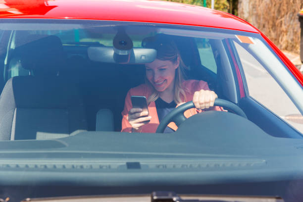 istock Young woman driving a car and using mobile phone 664627332