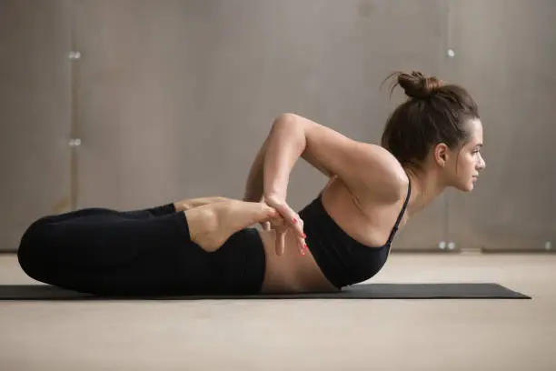 Photo of Young attractive woman stretching in Bhekasana pose, grey studio