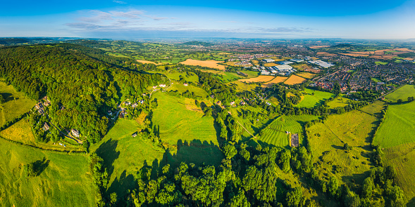 Aerial panoramic vista over green summer pasture, hedgerows and golden crops in this idyllic patchwork landscape of farmland surrounding suburban homes and country town.