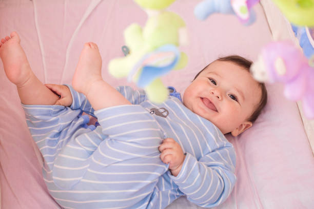 Happy baby lying in his crib smiling sticking his tongue at camera