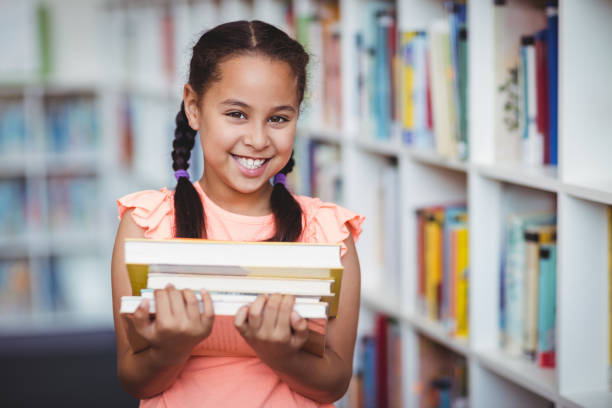 Cute girl holding books in a library. Young child doing research. Cute child doing her school work in a library. Mixed race child holding books