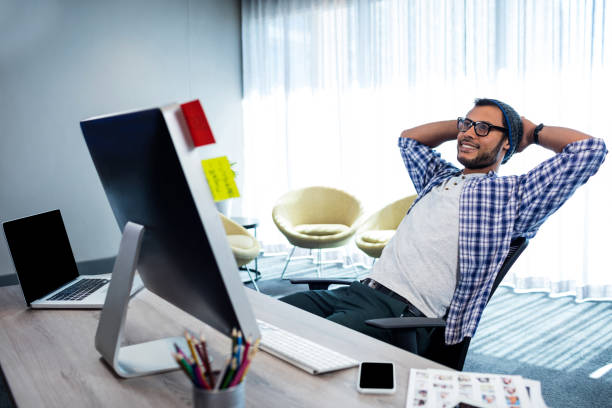 Smiling casual man with hands behind hand resting at desk in modern studio