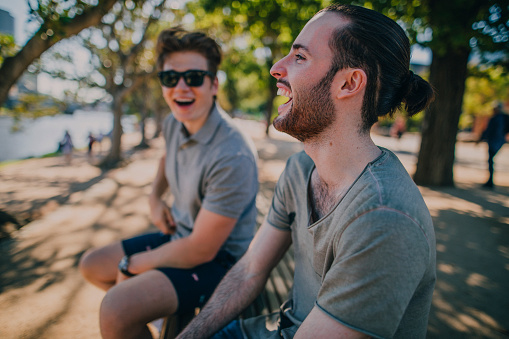 Two male friends laughing while sitting on a bench in Birrarung Marr in Melbourne, Australia.