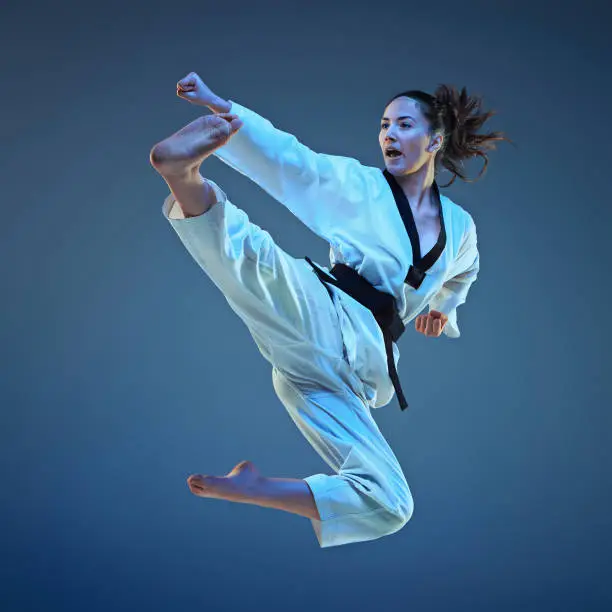 The karate girl with black belt jumping on blue background
