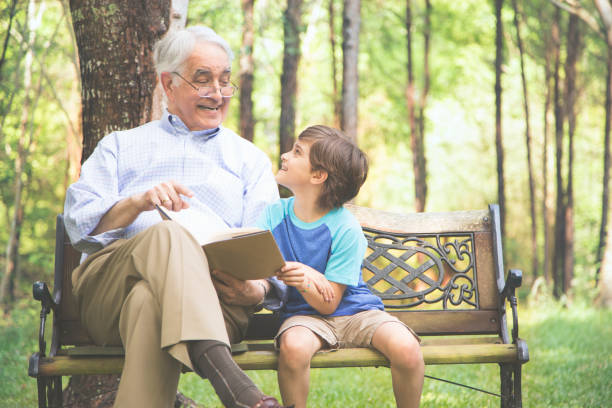 istock Grandfather and grandson reading books outdoors together. 664712992