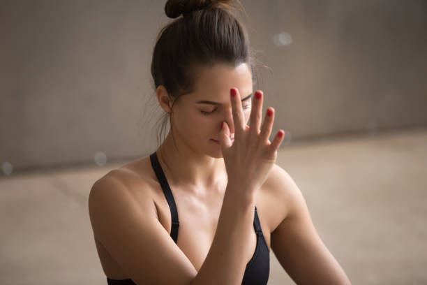 Young attractive woman making nadi shodhana pranayama, grey stud Young attractive yogi woman practicing yoga, using Alternate Nostril Breathing, making nadi shodhana pranayama therapeutic exercise, working out, cool urban style grey studio background, closeup, alternative pose photos stock pictures, royalty-free photos & images