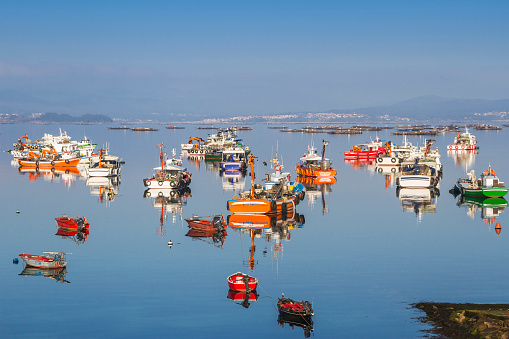 Reflected fishing and aquaculture boats on calm sea in Arousa Island with mussel rafts at background