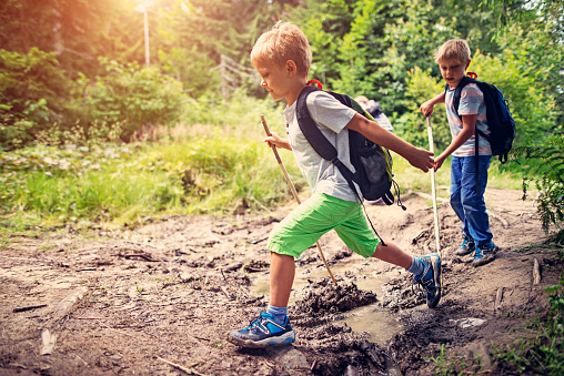 Little boys hiking in forest. jumping over stream on a muddy path. 
