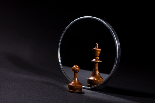 Pawn looking in the mirror and seeing a king. Black background.