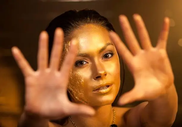 Portrait of beautiful woman with golden makeup and bodyart and outstretched forward arms. Focus on the face.