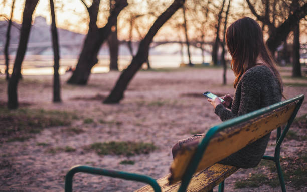 Young woman sitting on the bench typing a message stock photo