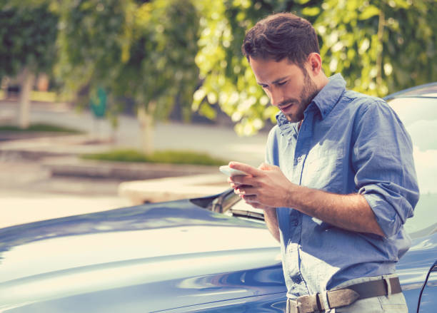istock Successful man standing by his car texting on mobile phone 664857754