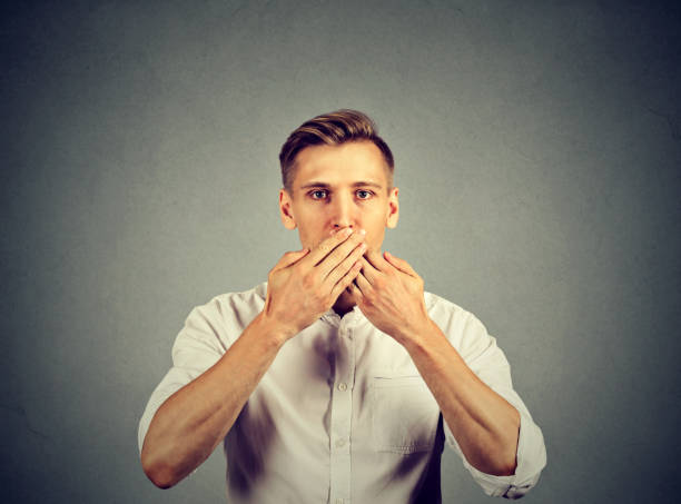 istock man with hands over his mouth, speechless isolated on gray wall background 664860456