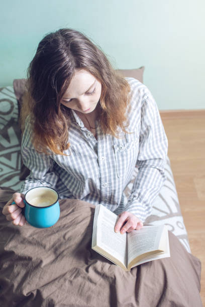 istock Cute girl reading a book while lying in bed 664868516