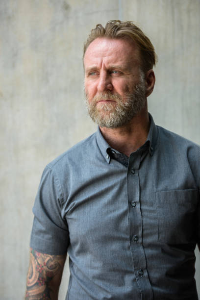 istock Mature bearded man with hand tattoos thinking against urban concrete wall 664871592