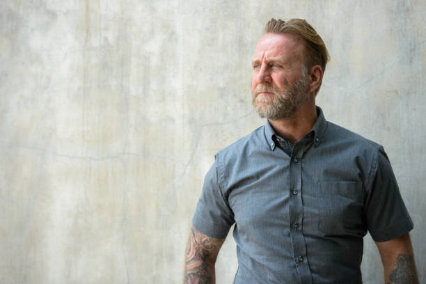 istock Mature bearded man with hand tattoos thinking against urban concrete wall 664871644