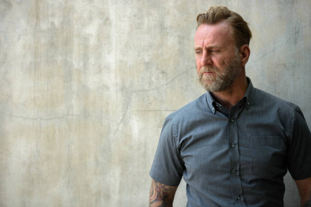 istock Mature bearded man thinking with hand tattoos against urban concrete wall 664871792