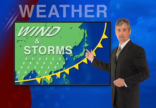 A tv television news weather man meteorologist anchorman is reporting with a Wind & Storm graphic over a map of Asia on the monitor screen.