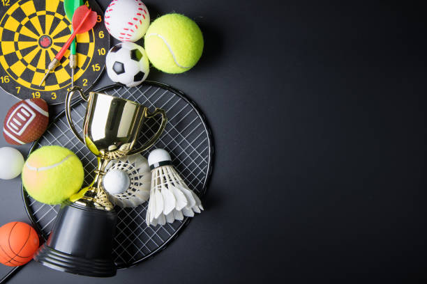 trofeo d'oro, freccette, racket ping pong, ping pong ball, shuttlecocks, racchetta badminton e palla da tennis su sfondo nero. concetto sportivo, vincitore del concept, copia l'immagine dello spazio per il tuo testo. - rubber dart foto e immagini stock