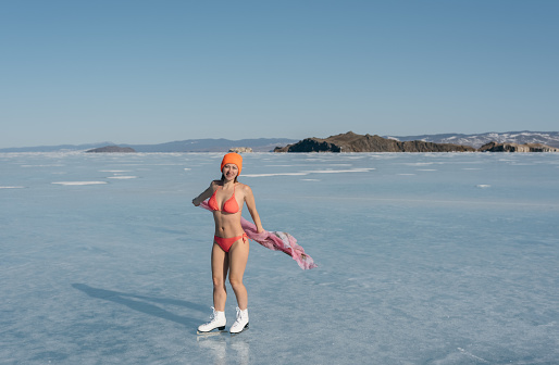 Girl extreme sportswear in a swimsuit on the ice. Ice lady. A female beginner skater skates and poses on skates, and tans. She has a beautiful body, strong health and great courage. It's freezing outside.