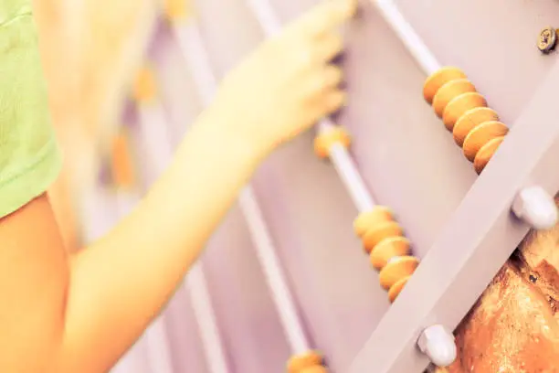 Child plays with wooden abacus. Orange wall. Hands.