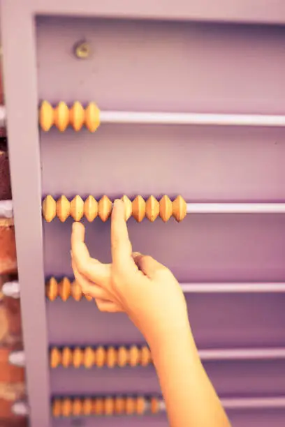 Child plays with wooden abacus. Orange wall. Hands.