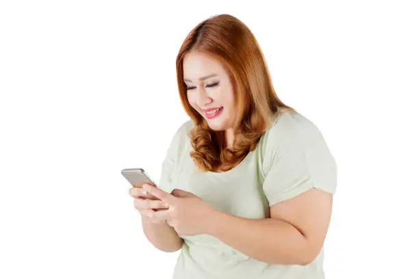 Portrait of blonde woman with overweight body, texting on her smartphone. Isolated on white background