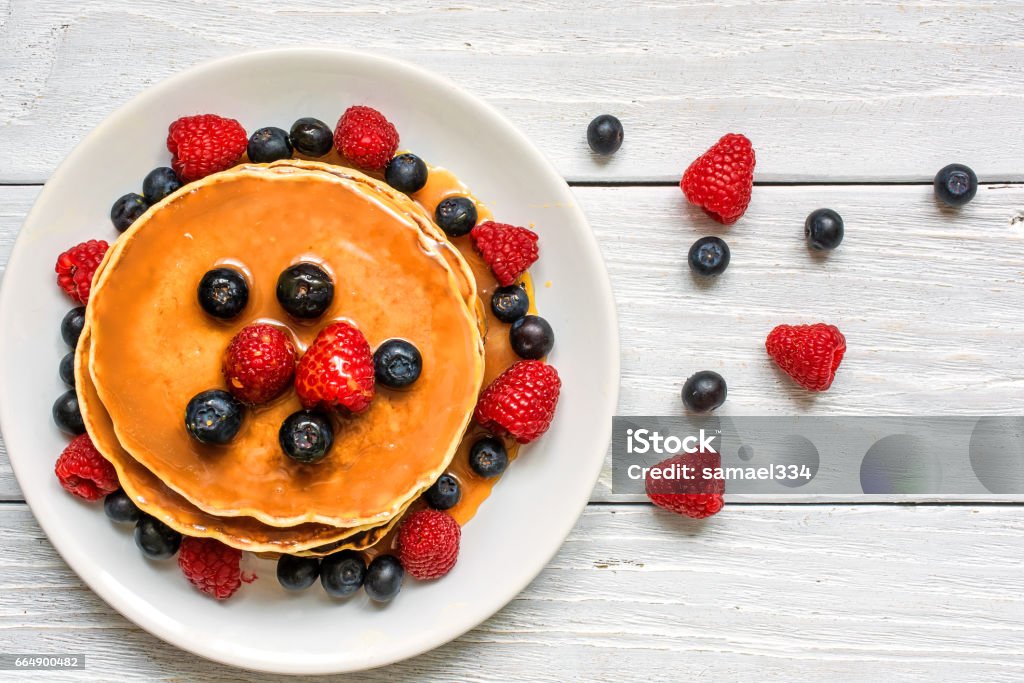 stack of pancakes with fresh berries and caramel sauce stack of pancakes with fresh berries and caramel sauce on white wooden background. top view Pancake Stock Photo