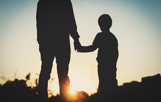 silhouette of father and son holding hands at sunset sky