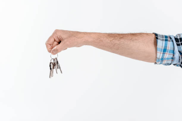 A close-up of a man holding a set of keys infant of a door with brass doorknob