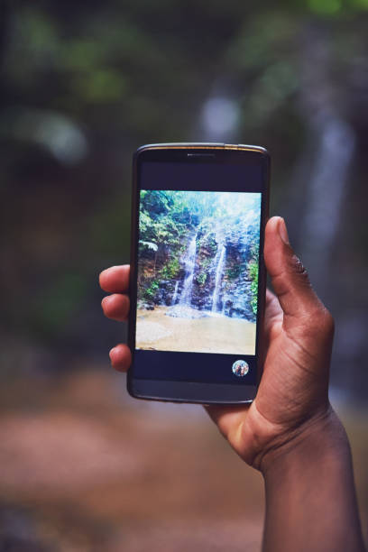 Shot of an unidentifiable young tourist taking a picture of a waterfall with his smartphone