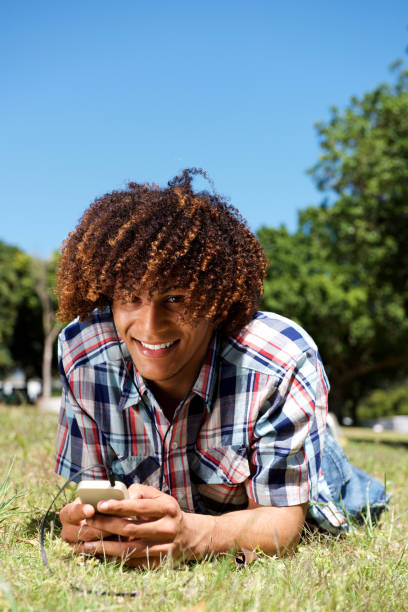 istock smiling young afro man lying down on grass in park holding phone 664934140