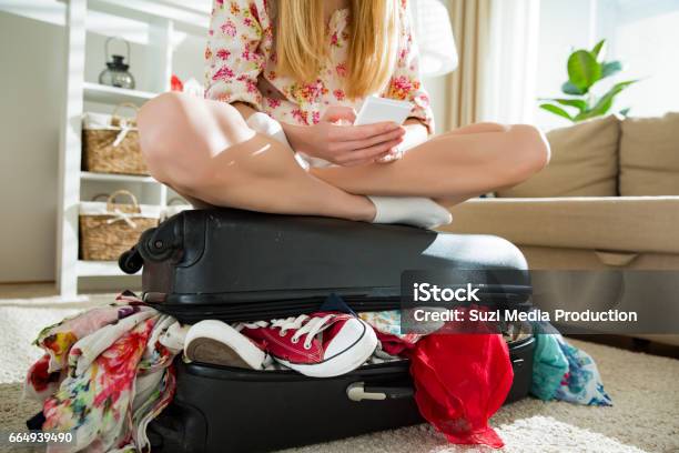 Happy Young Woman In Colorful Summer Outfit Sitting On Staffed Suitcase With Smart Phone Stock Photo - Download Image Now
