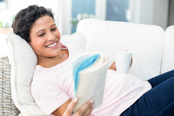 istock Pregnant woman reading book while holding coffee cup 664946288