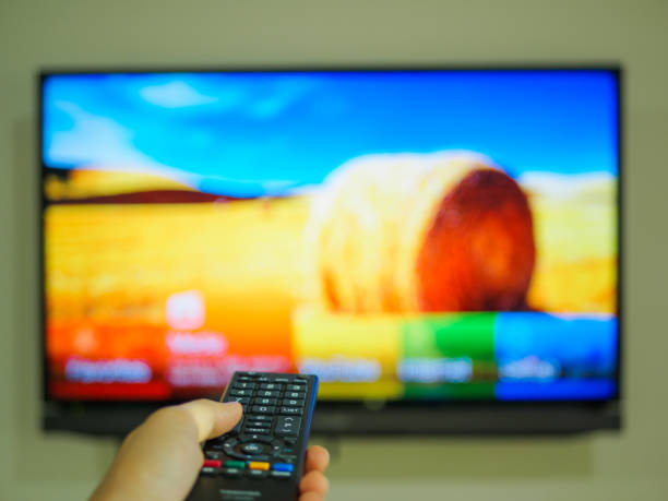istock Close up Hand holding TV remote control with a television in the background. 664947070