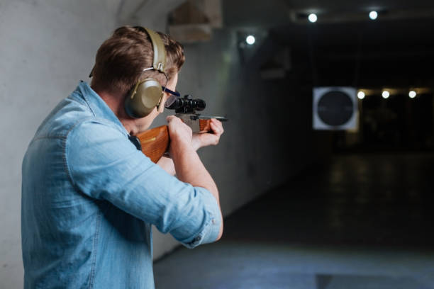 Handsome serious man looking at the target Hitting the bulls eye. Handsome confident serious man holding the rifle and looking into the target while trying to hit the bulls eye target shooting stock pictures, royalty-free photos & images