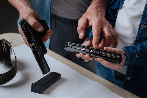 Handgun construction. Nice pleasant handsome man standing near his daughter and pointing at the handgun spring while showing her the construction of a gun