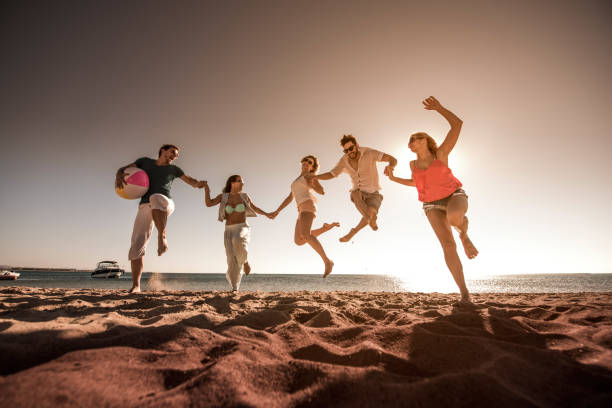 istock Young happy people holding hands and jumping on the beach. 664968536