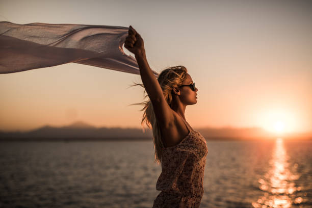 istock Beautiful woman with shawl on a windy day at sunset. 664972392
